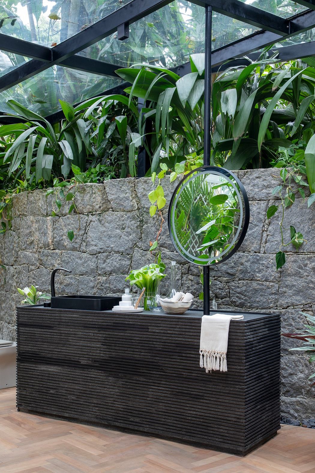 Modern bathroom vanity against a stone wall with greenery under a glass roof.