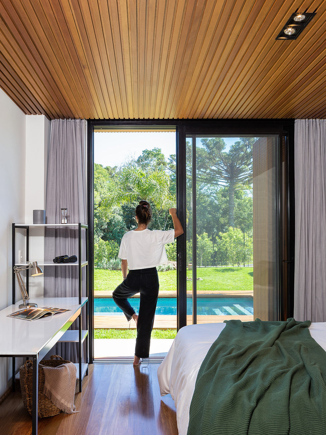 Modern bedroom with wood ceiling, large window, and person looking outside.