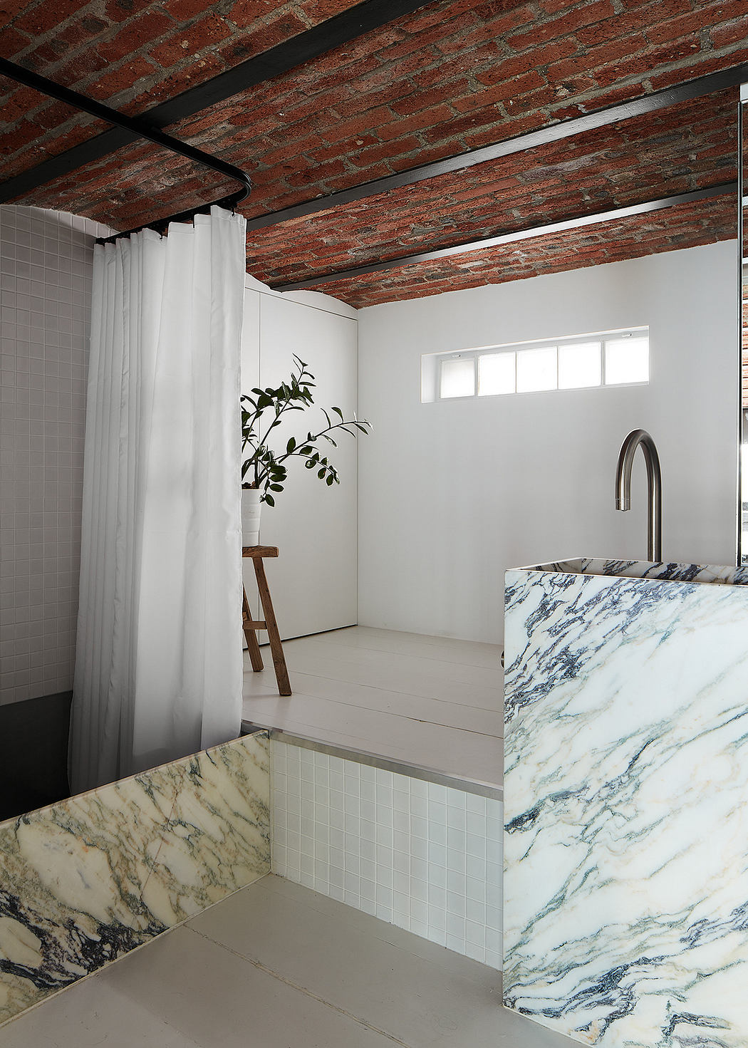 Minimalist bathroom with marble details and exposed brick ceiling.