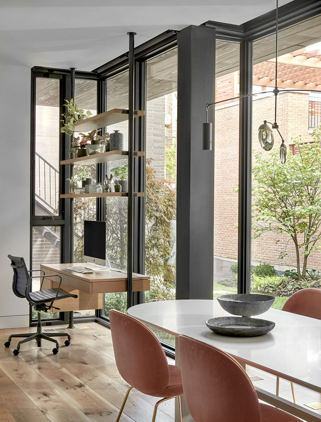 Modern home office with glass walls, wooden floors, and a view of greenery