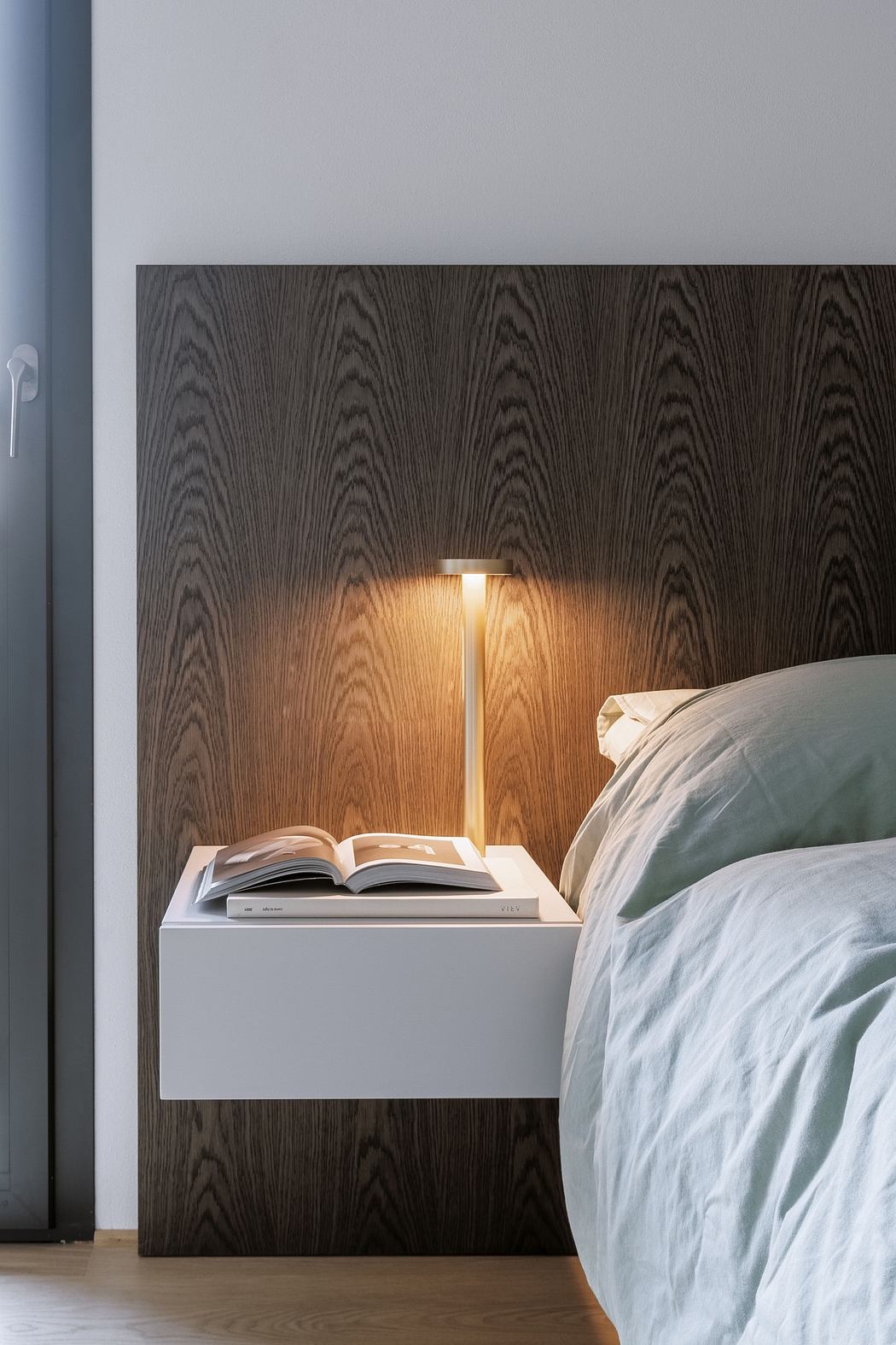Modern bedroom with dark wood paneling, a stylish lamp, and an open book