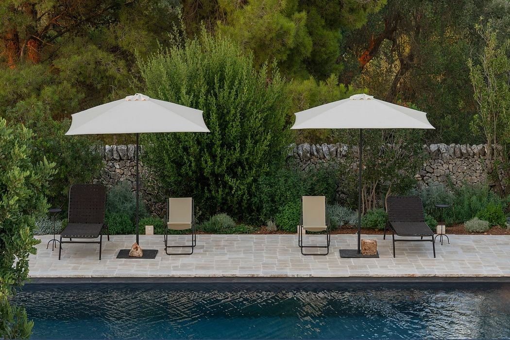 A serene poolside with loungers, umbrellas, and lush green backdrop.