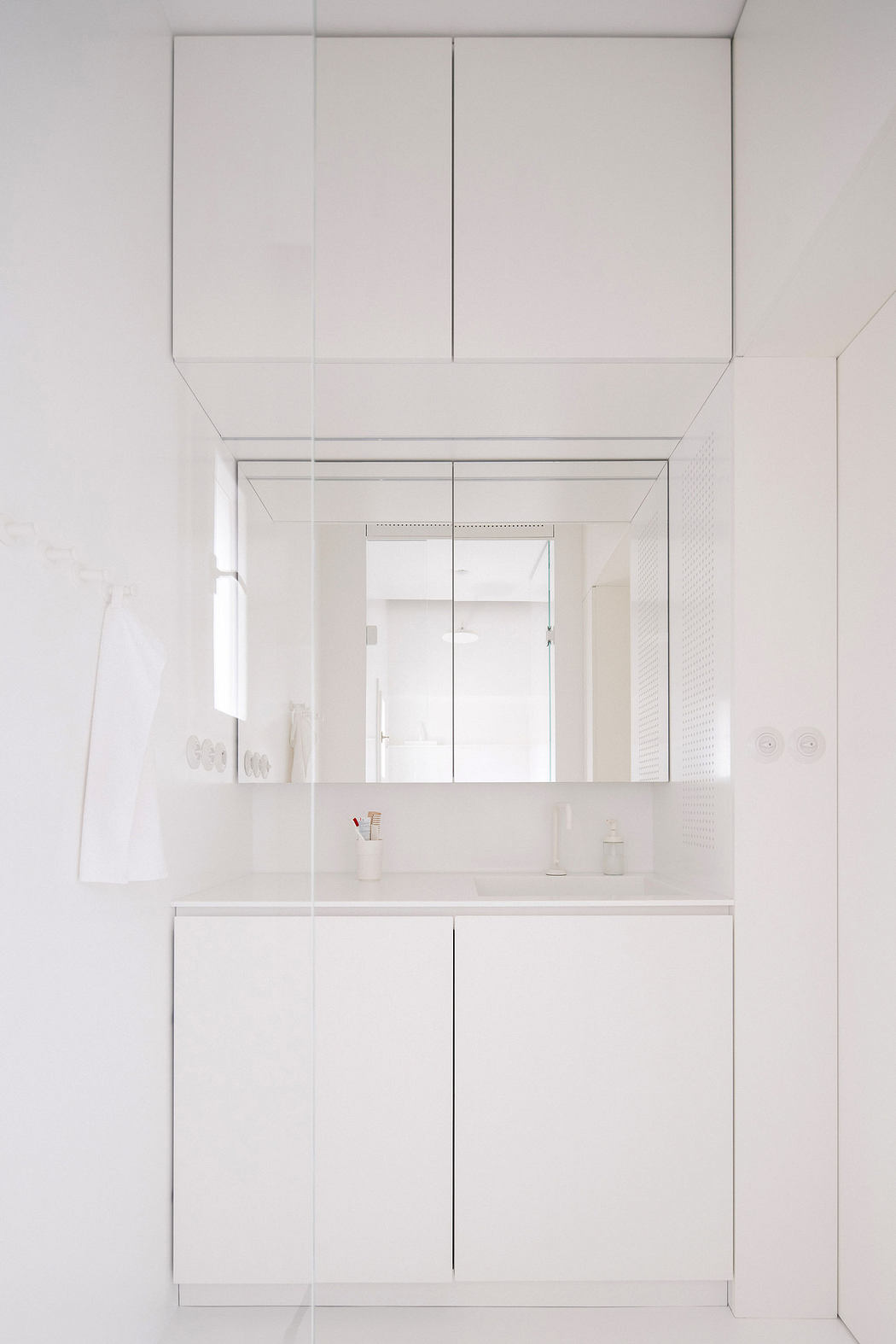 Minimalist white bathroom cabinetry with a mirrored wall cabinet.