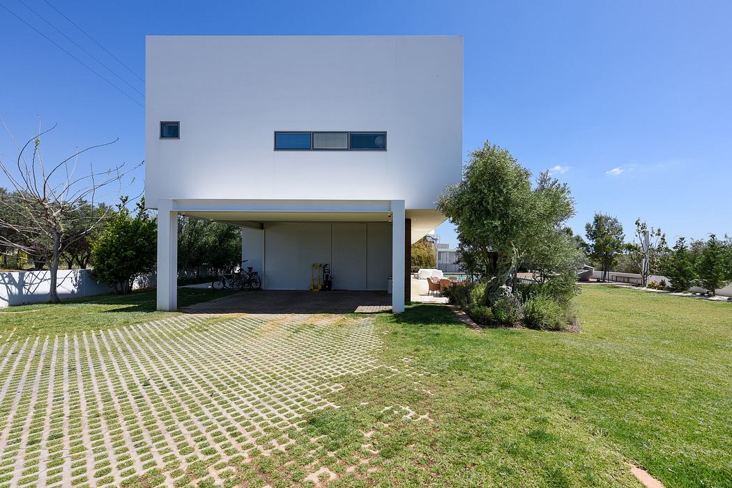 Modern white cubic house with open carport and green lawn.