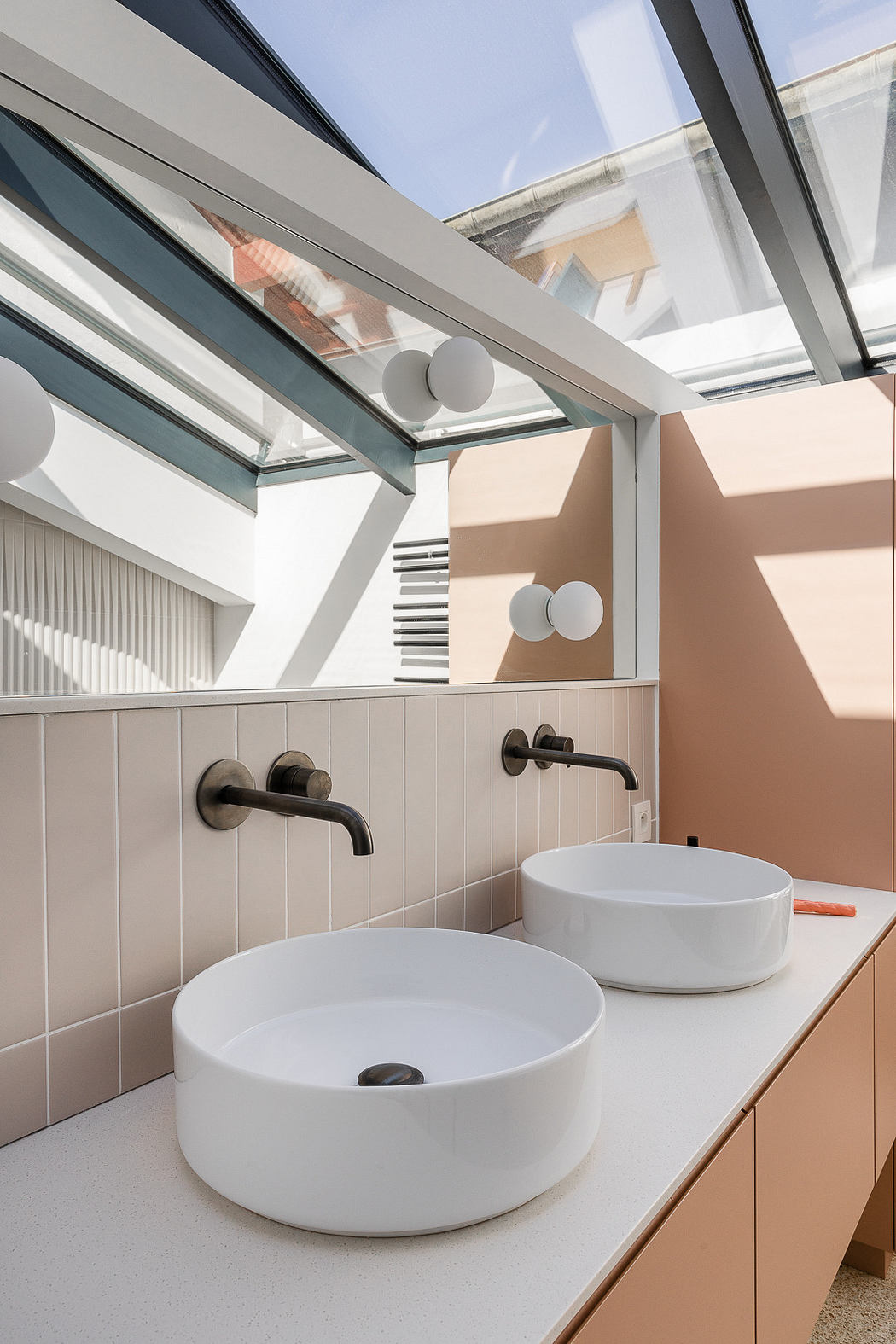 Modern bathroom with skylight, two vessel sinks, and pastel colors.