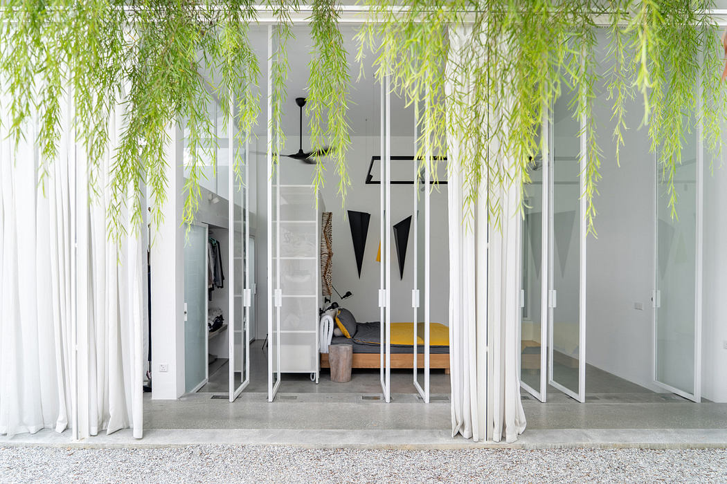 Modern white room with hanging greenery and minimalist decor viewed through vertical bars.