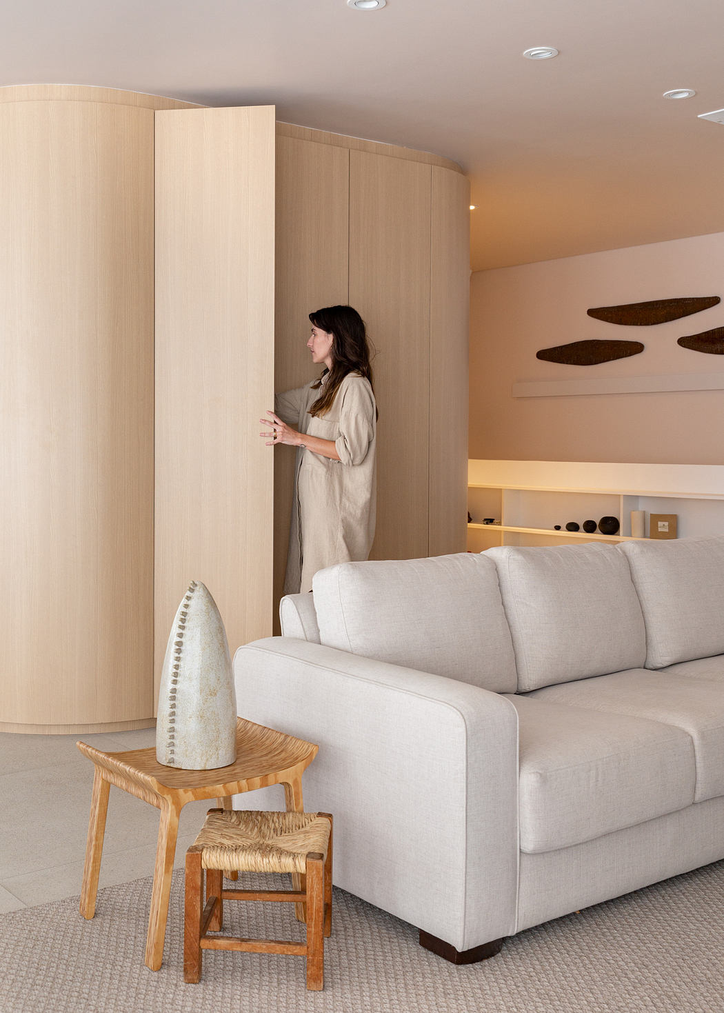 Modern living room with curved wood panels, a woman standing, a sofa, and