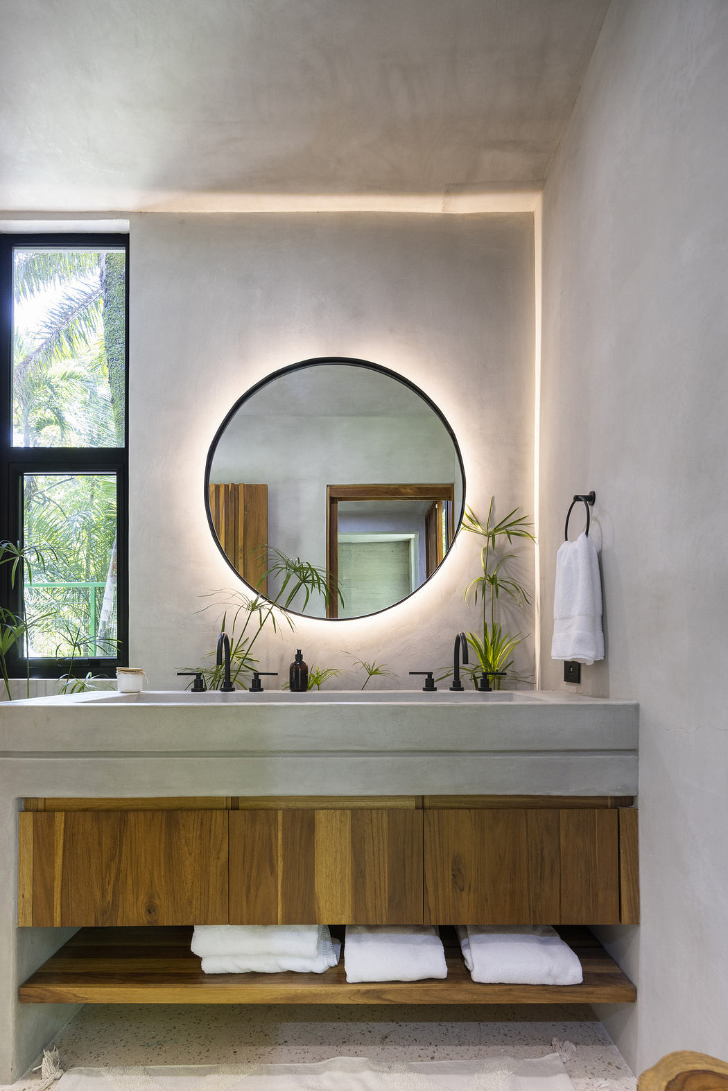 Modern bathroom with round mirror, wooden vanity, and white towels.