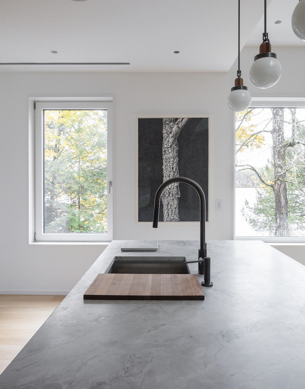 Modern kitchen with a minimalist design, pendant lights, and a window view of trees