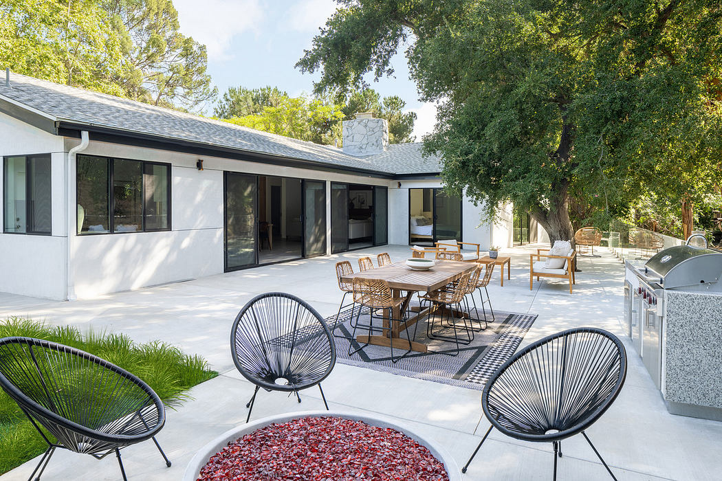 Modern patio with outdoor dining area and wire chairs beside a white house.