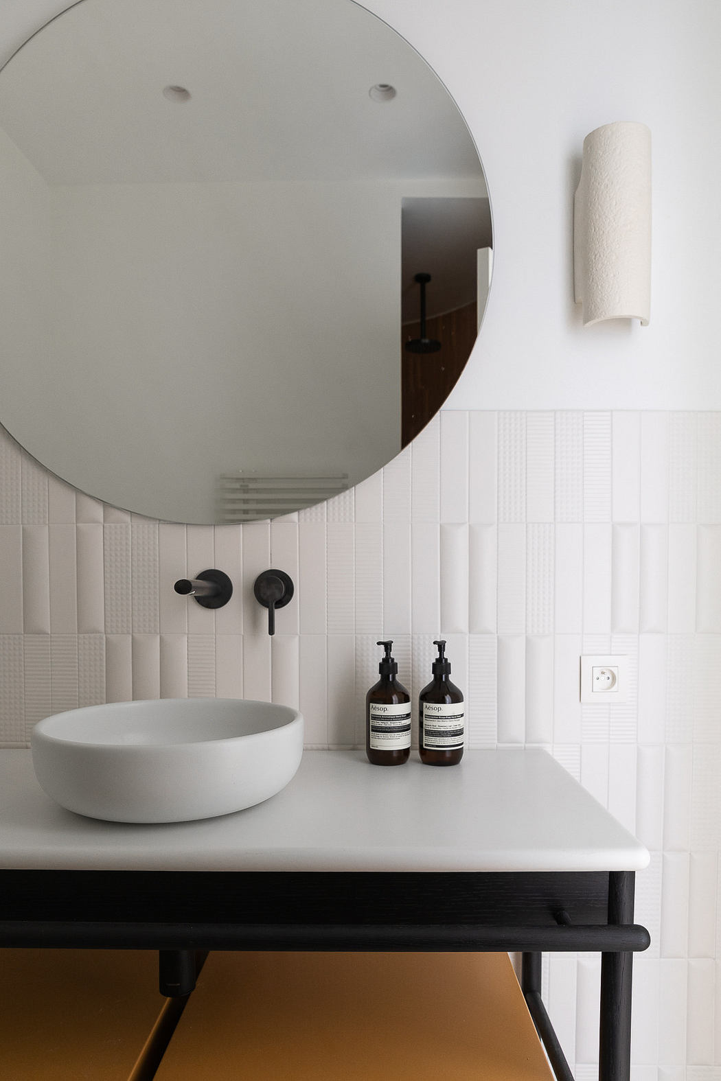 Minimalist bathroom with round mirror, white basin, and black fixtures.