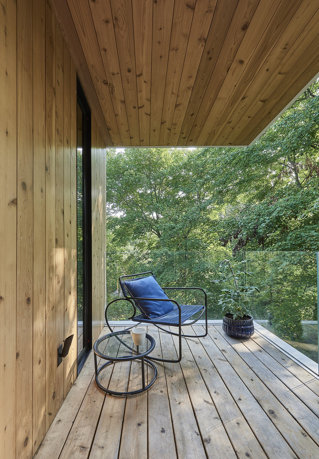 Modern wooden balcony with a metal chair and forest view.