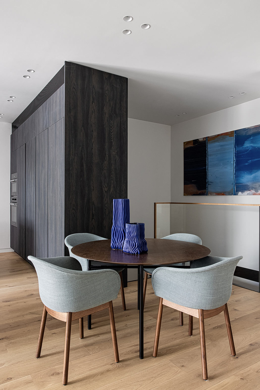 Modern dining room with wooden table, pastel chairs, and abstract art.