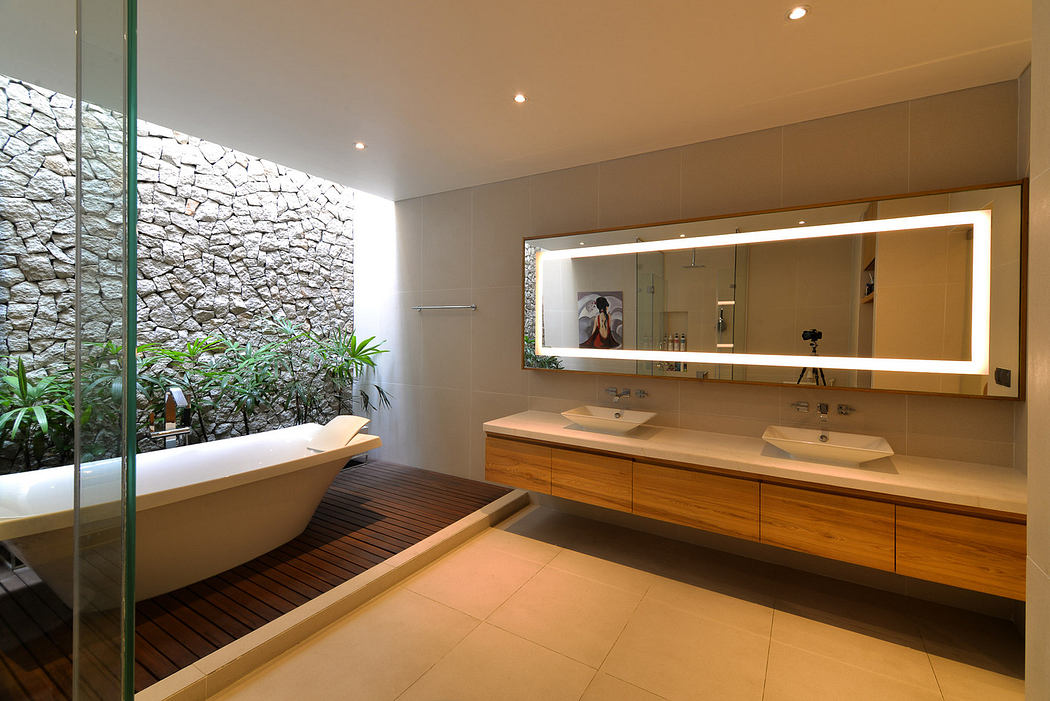 Modern bathroom with a freestanding tub, stone wall, and large mirror.