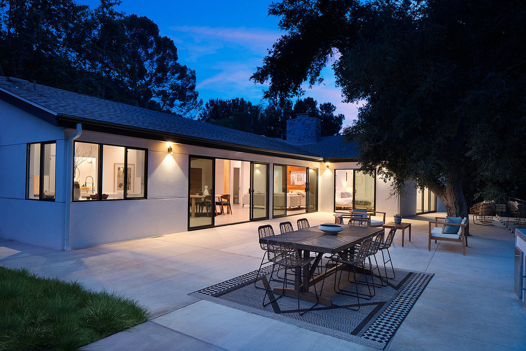 Modern house exterior at dusk with lit interior and patio dining set.
