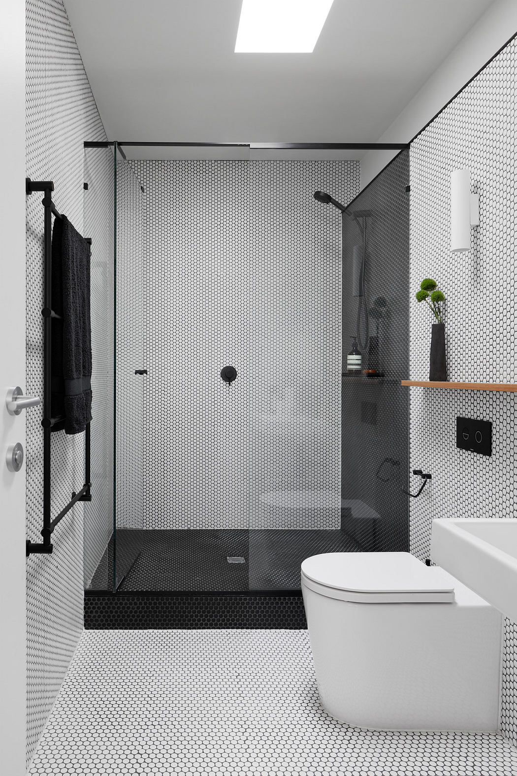 Modern bathroom with black and white mosaic tiles, glass shower, and minimalist fixtures.