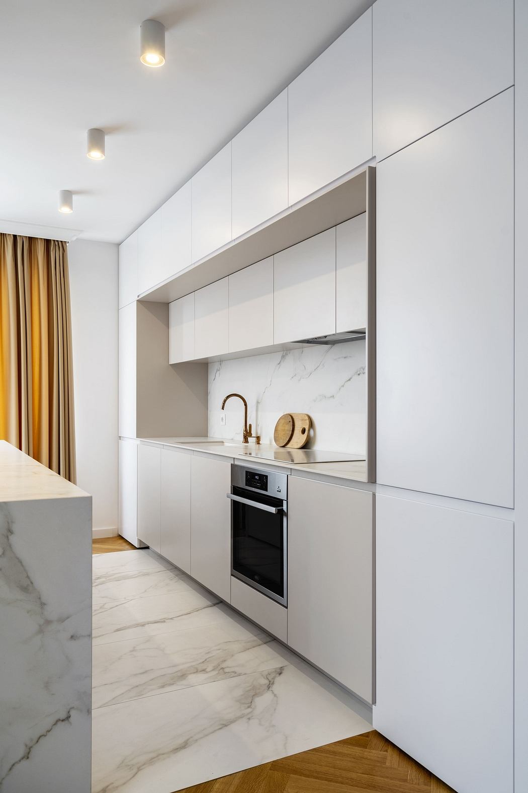 Modern kitchen with white cabinets, marble countertops, and wooden floor.