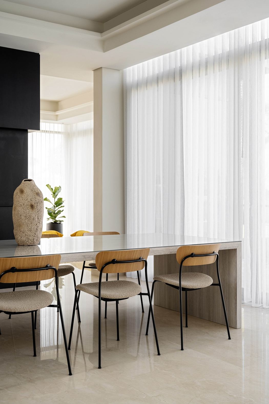 Modern minimalist dining area with sleek table, wooden chairs, and sheer curtains.
