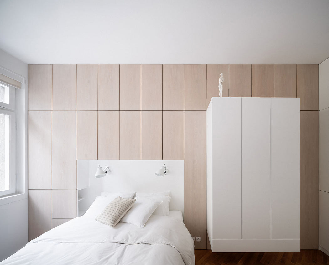Minimalist bedroom with wooden panel wall and white bed.