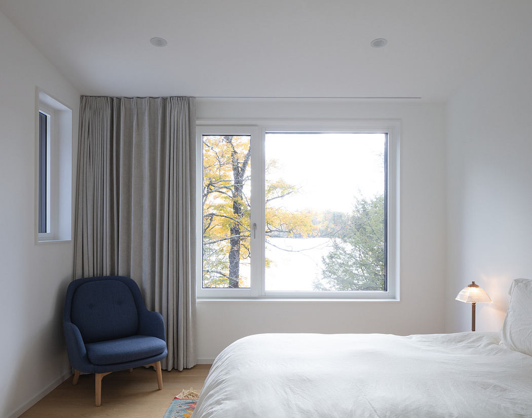 Minimalist bedroom with large window overlooking autumn trees.