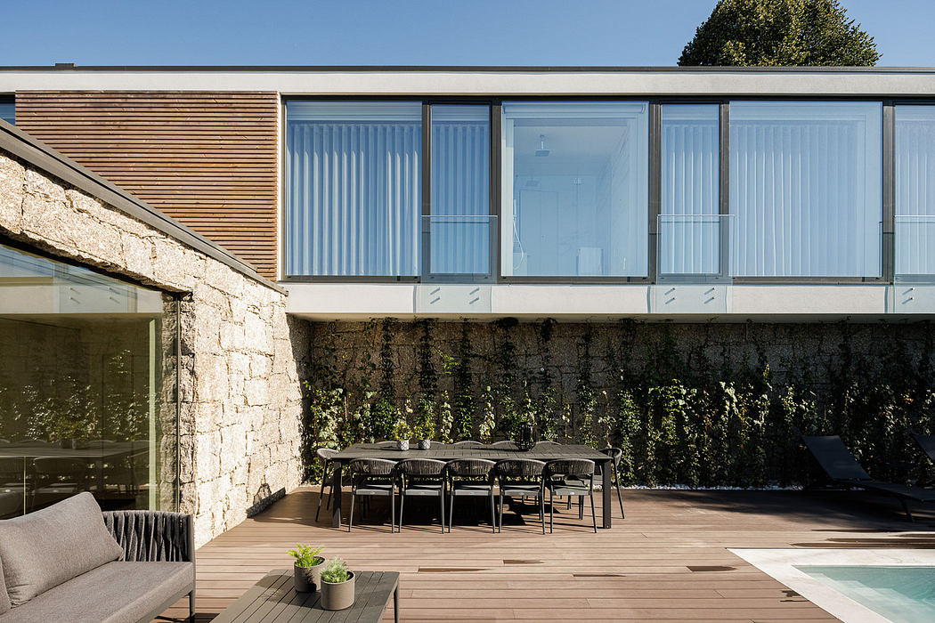 Modern house exterior with stone walls, glass facade, and outdoor furniture on patio.