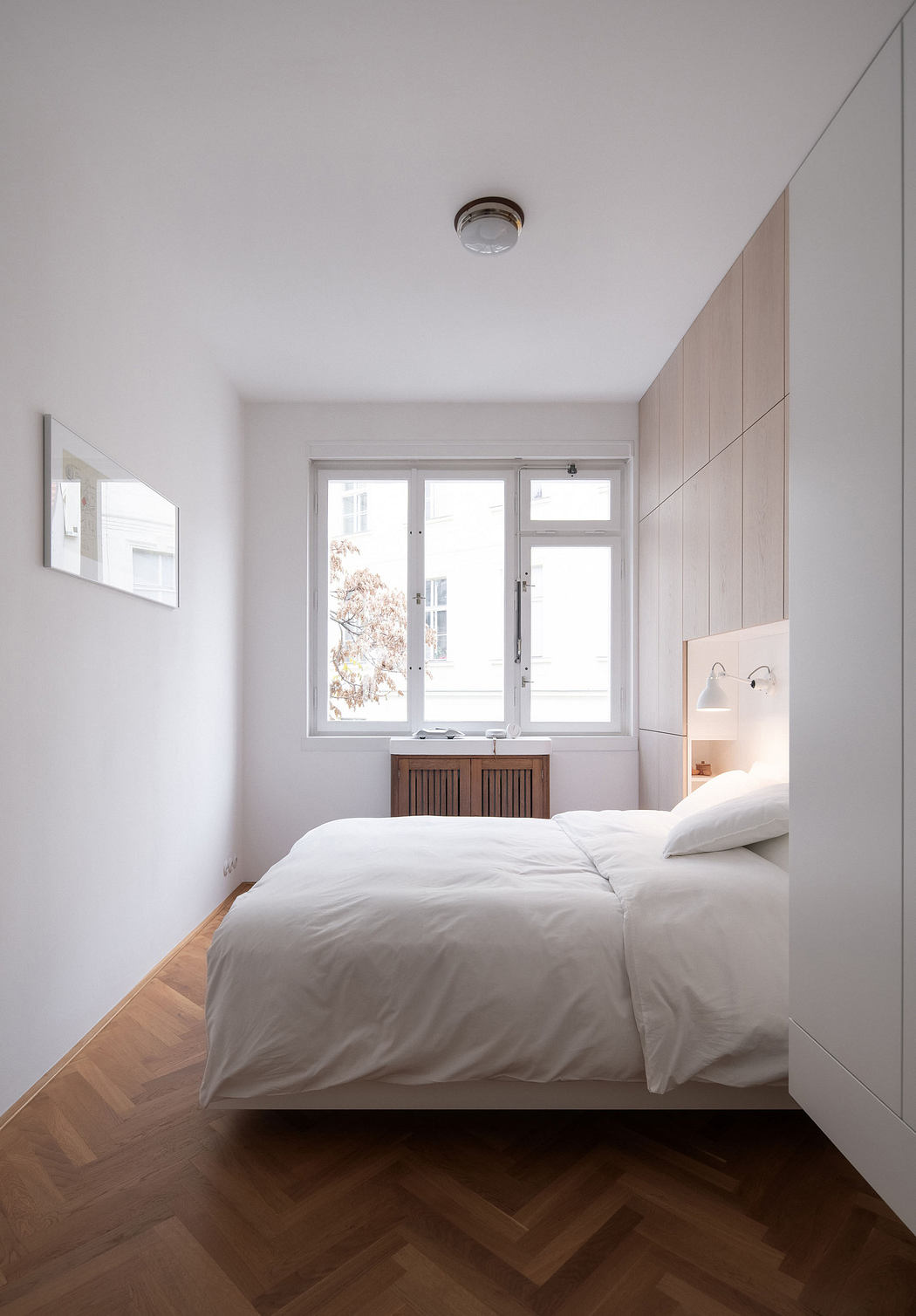 Minimalist bedroom with wooden floor, white bedding, and built-in cabinets.