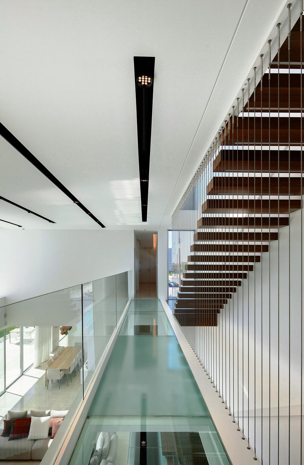 Modern interior with a glass floor walkway and wooden staircase.