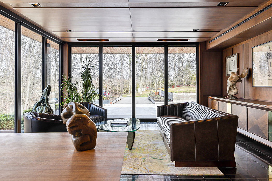 Modern room with glass walls, wooden panels, leather sofas, and artwork.