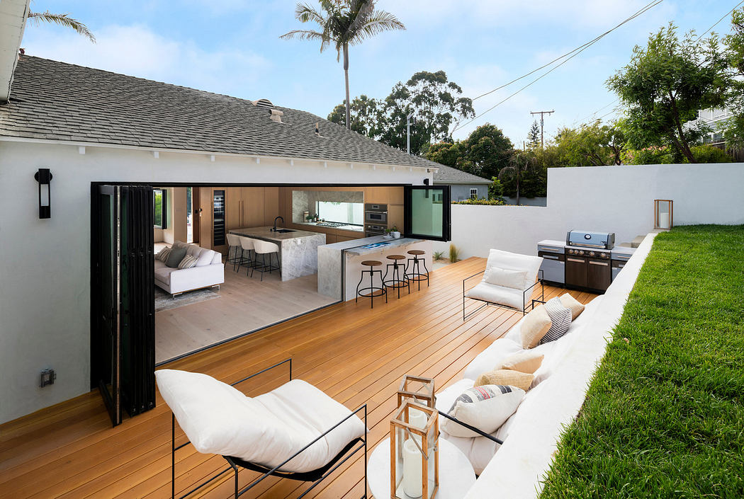 Modern backyard patio with open living space, wooden deck, and white furnishings.