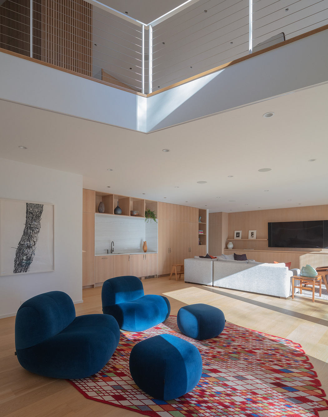 Modern living room with blue beanbags, colorful rug, and high ceiling.