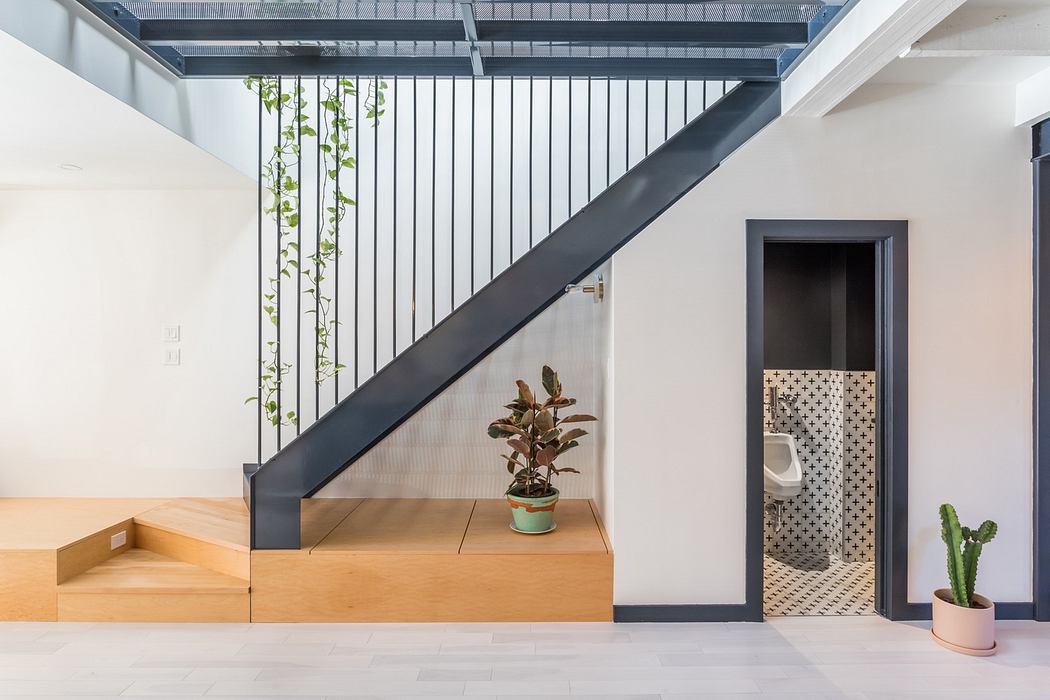 Modern stairwell with wooden steps, black railing, and indoor plants.