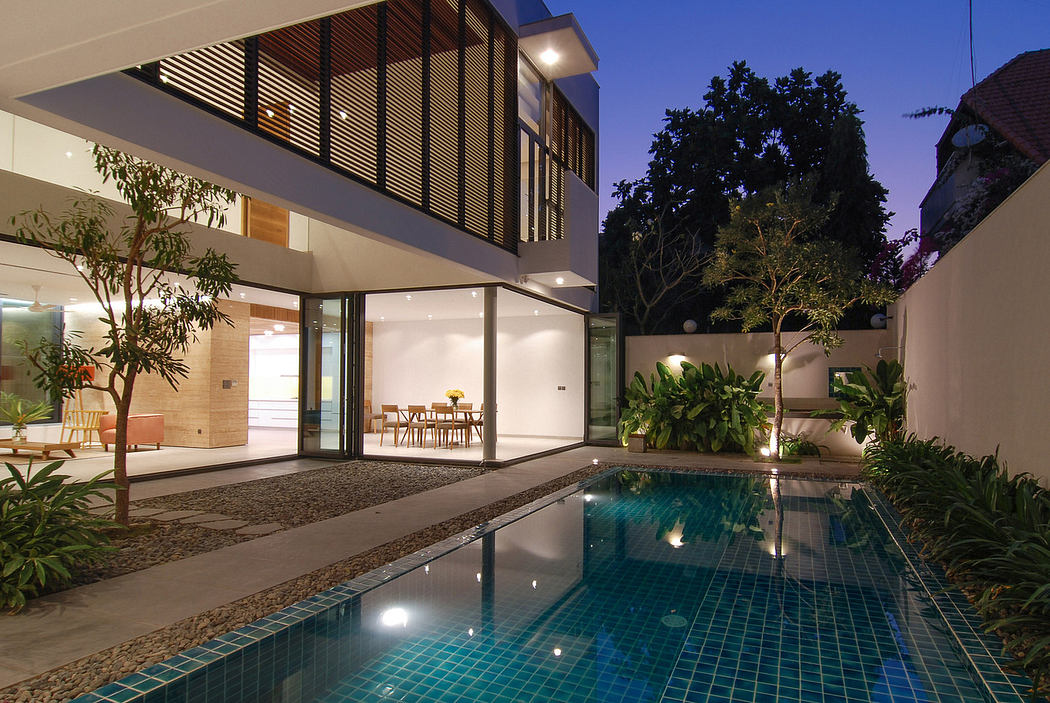 Modern house with pool at twilight, large windows, and outdoor dining.