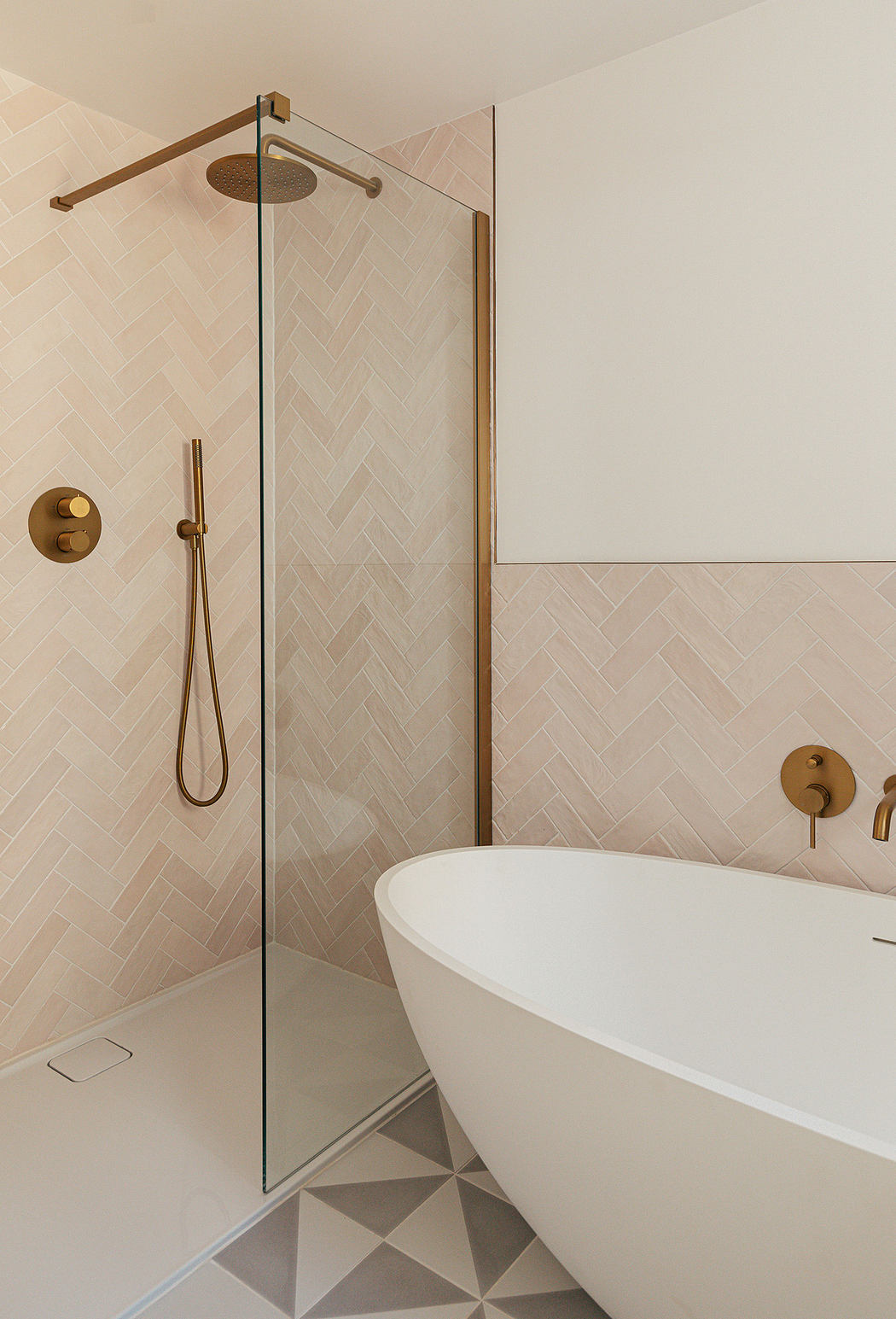 Modern bathroom with herringbone tiles, glass shower, and freestanding tub