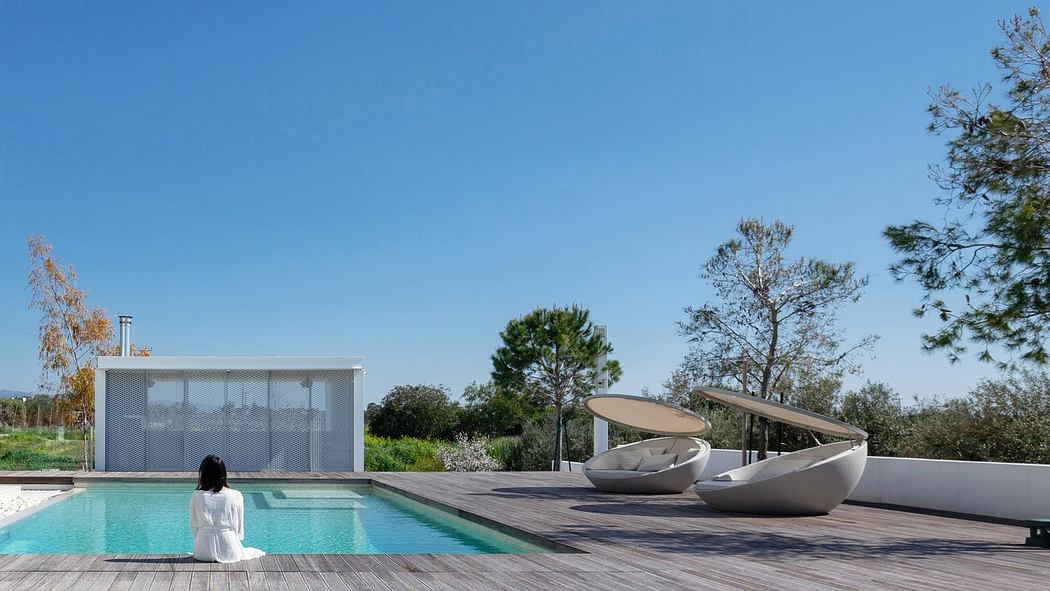Modern poolside with wooden decking, loungers, and glass house under clear blue