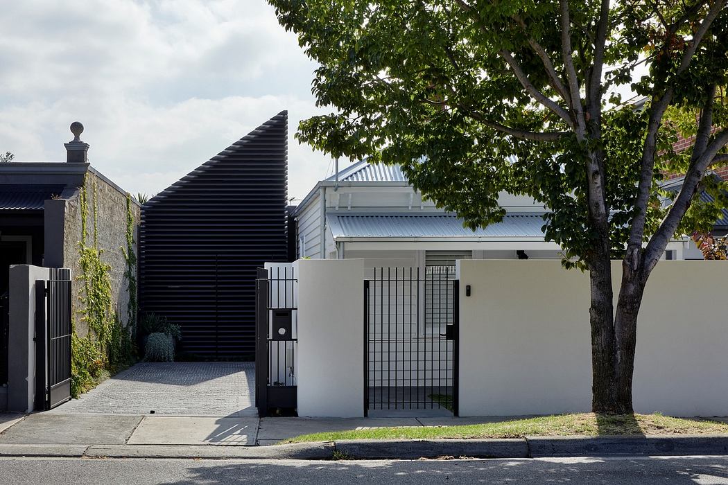 Modern house facade with contrasting textures and gated entry.
