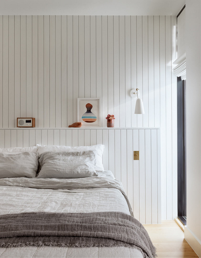 Minimalist bedroom with white paneled walls, cabinet and cozy bedding.