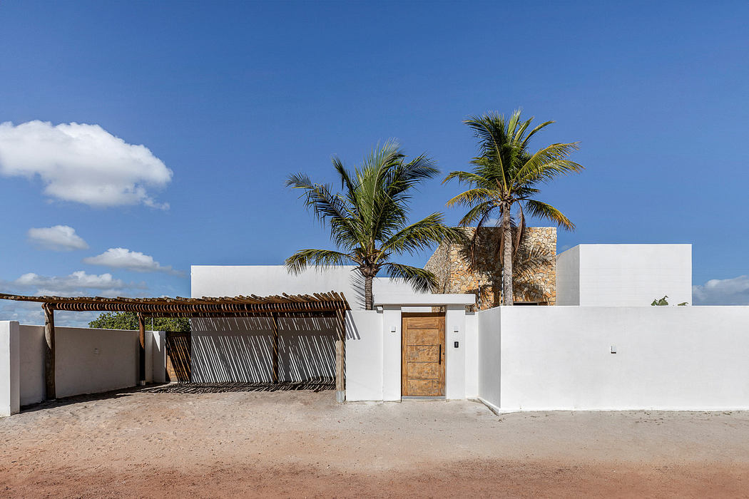 Modern white house with a thatched entryway and palm trees against a blue sky