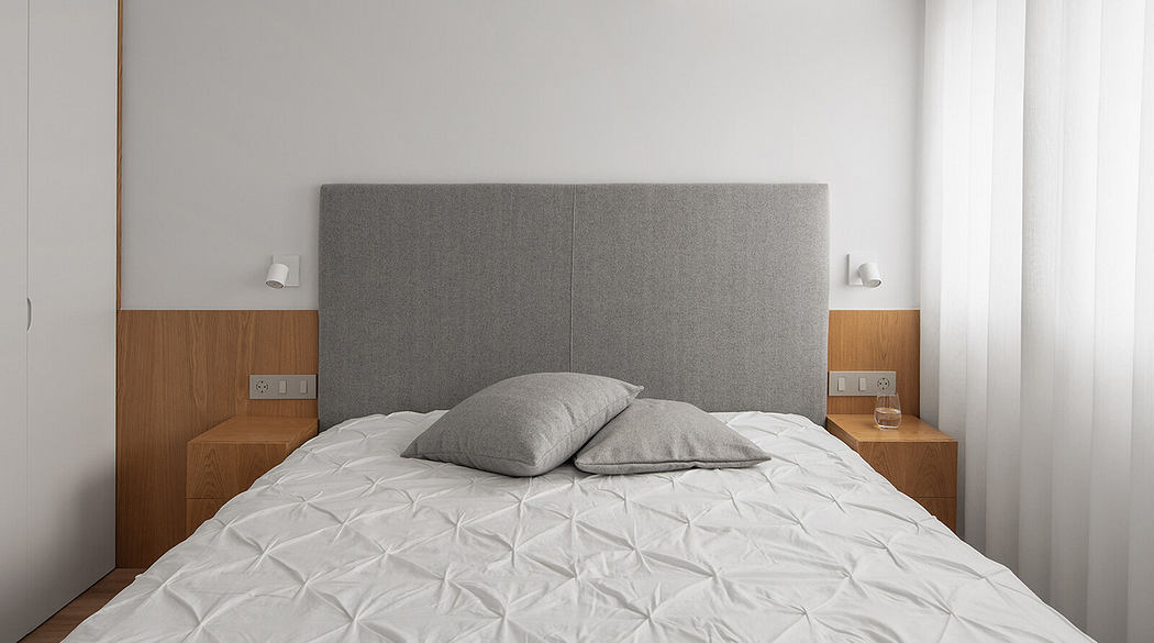 Minimalist bedroom with a large bed, grey headboard, and wooden accents.