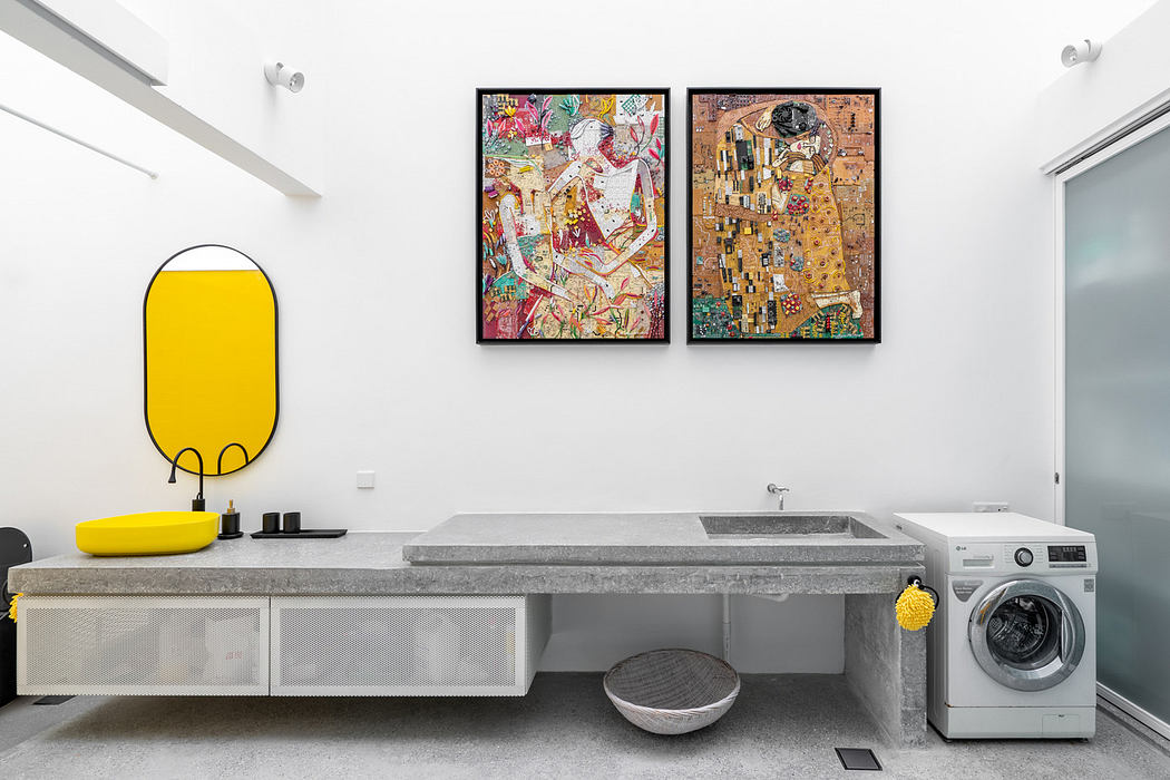 Modern laundry room with bright artworks, concrete countertop, and yellow accents.