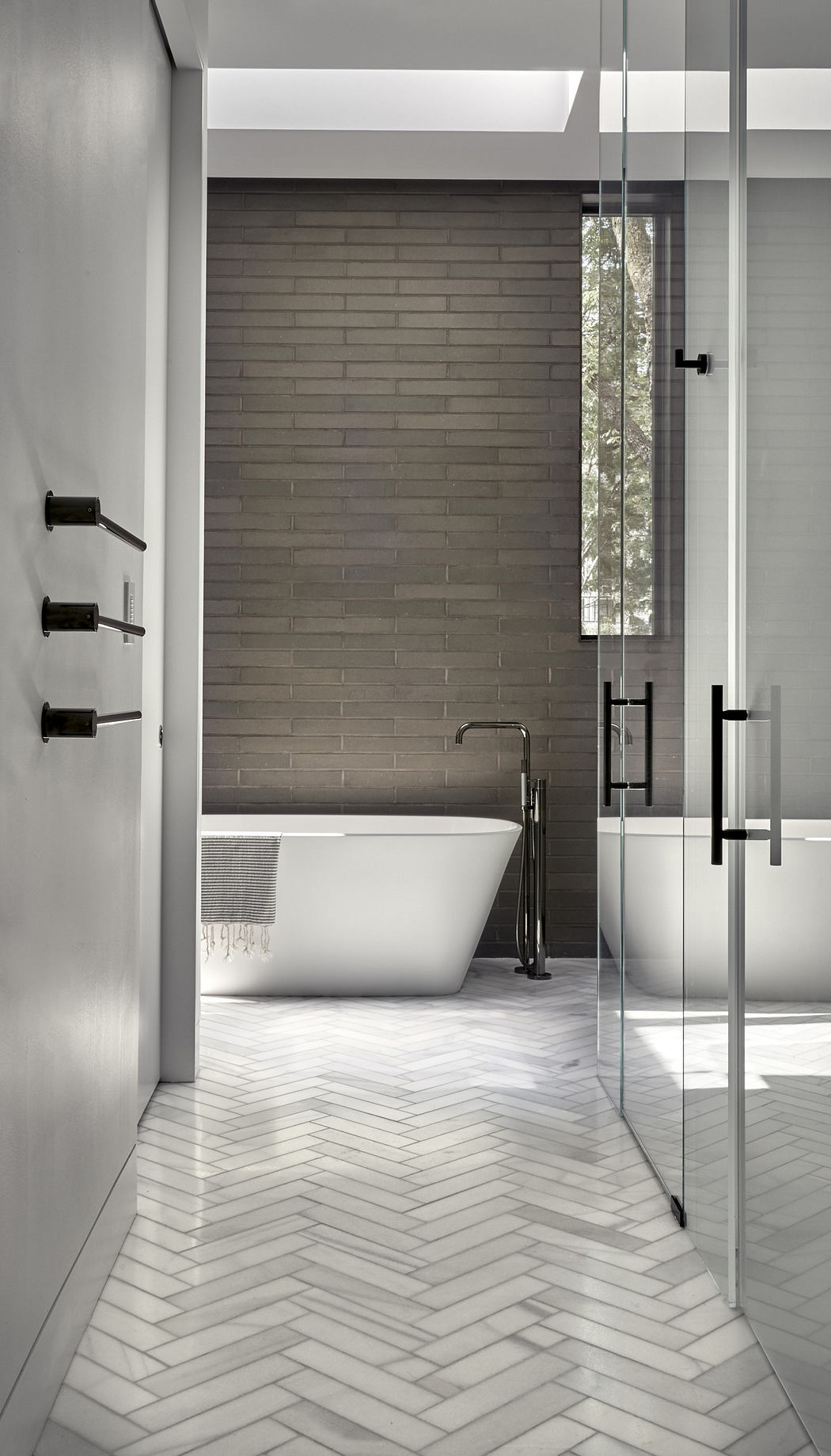 Modern bathroom with herringbone floor tiles and glass shower.