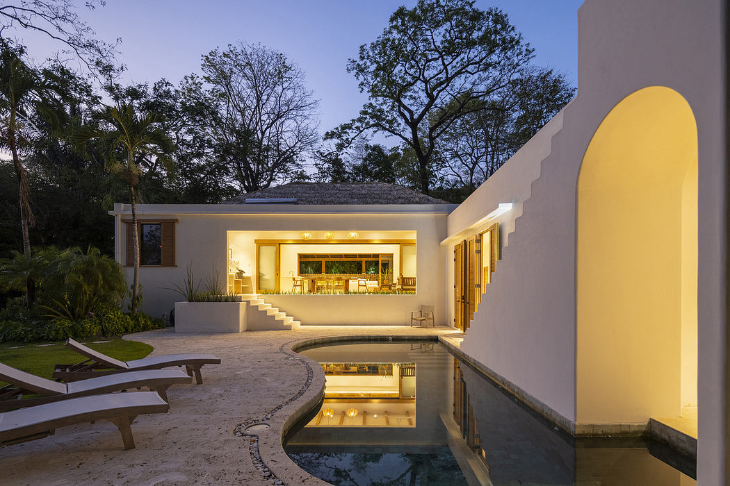 Modern house with illuminated interiors, poolside loungers, and a twilight sky.