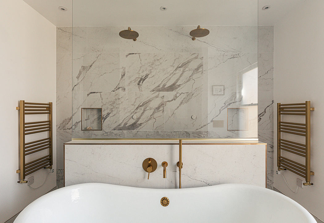 Modern bathroom with marble walls, white tub, and brass fittings.