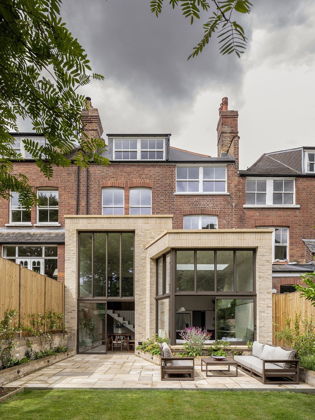 Modern two-story home extension with glass facade and patio furniture.