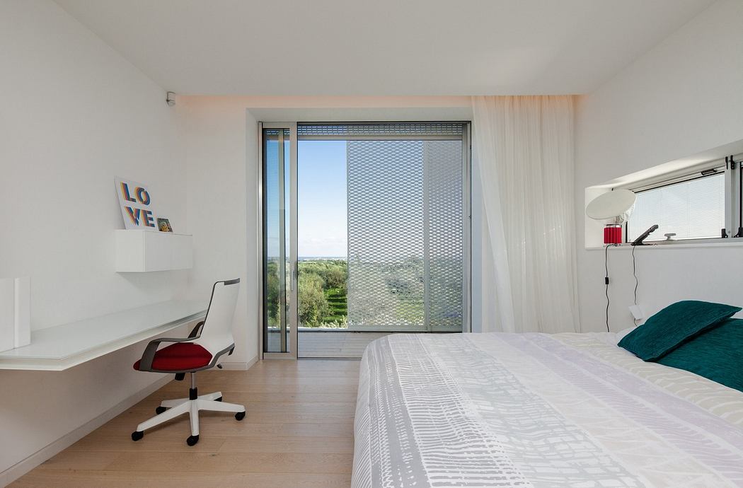 Modern minimalist bedroom with a white desk, bed, and sliding door to balcony.