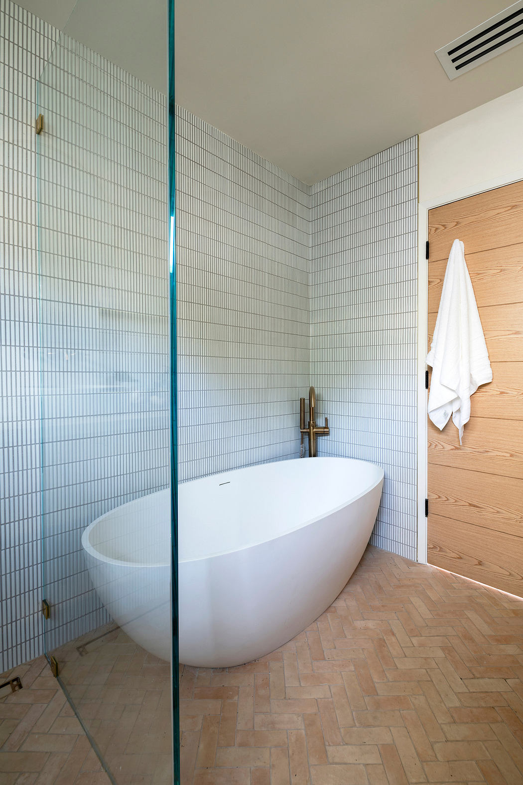 Modern bathroom with white freestanding tub, herringbone wood floor, and
