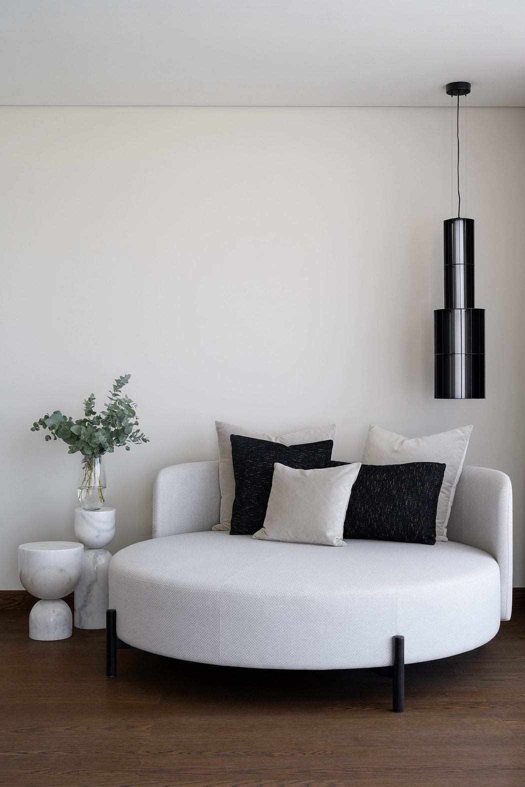 Minimalist living room with white sofa, pendant light, and plant.
