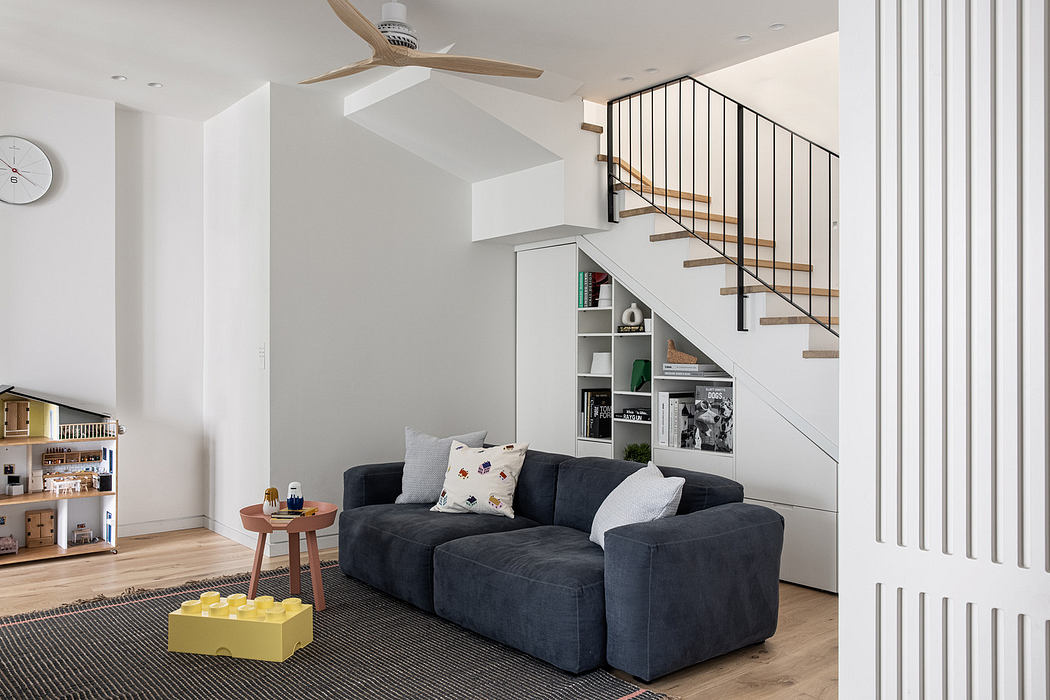 Modern living room with a blue sofa, wooden stairs, and neutral decor.