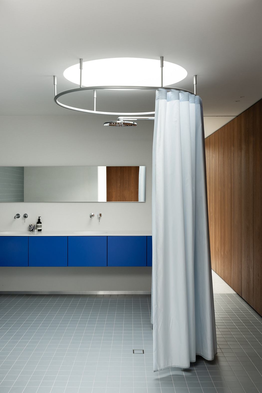 Modern bathroom with wooden cabinets, blue vanity, and round shower curtain.