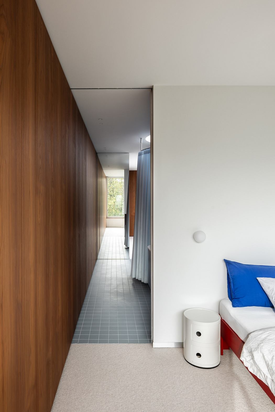 A modern bedroom with wooden paneling and a view into a tiled hallway.