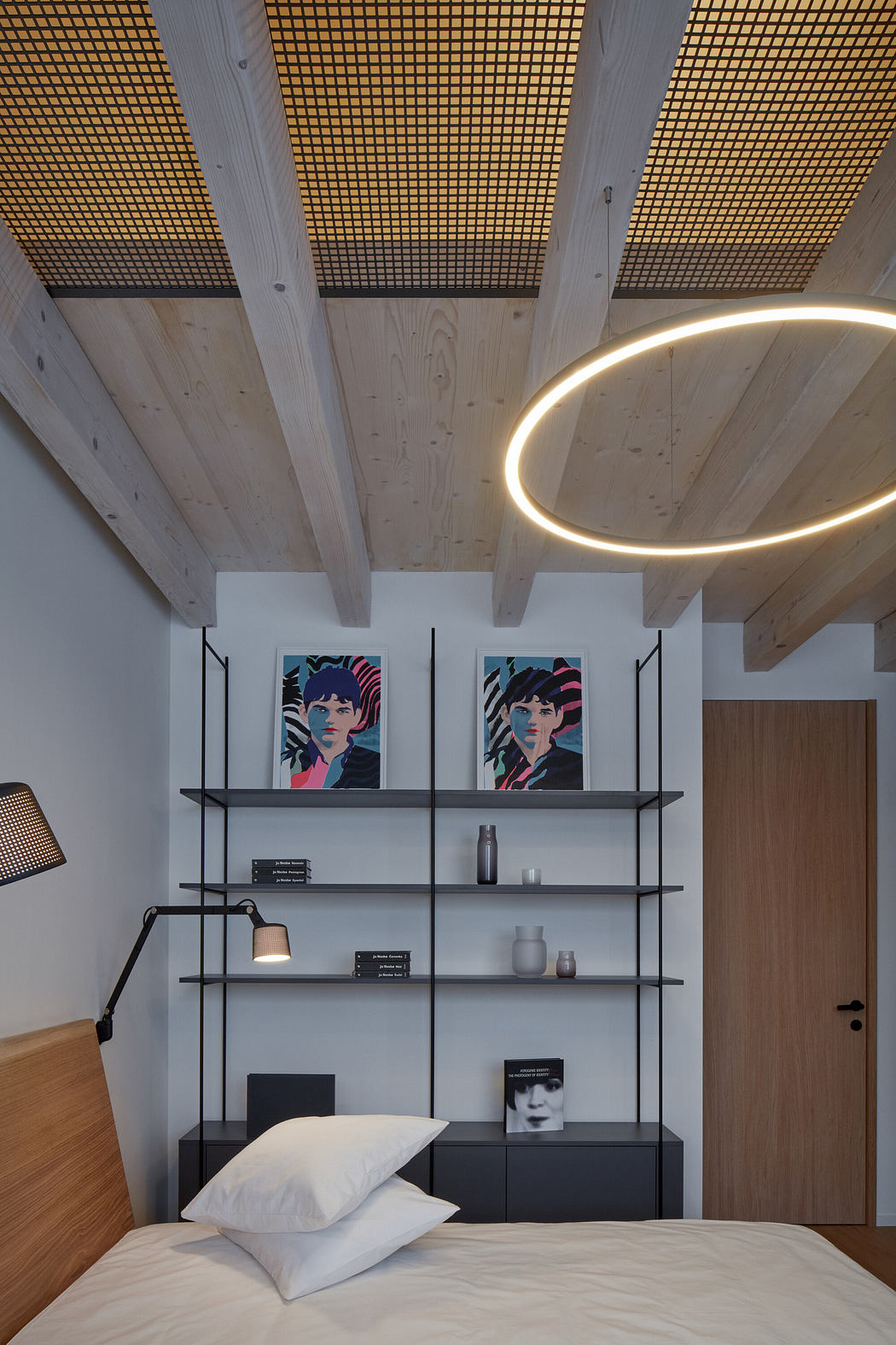 Modern bedroom with wooden ceiling, circular light fixture, and artwork above shelving.